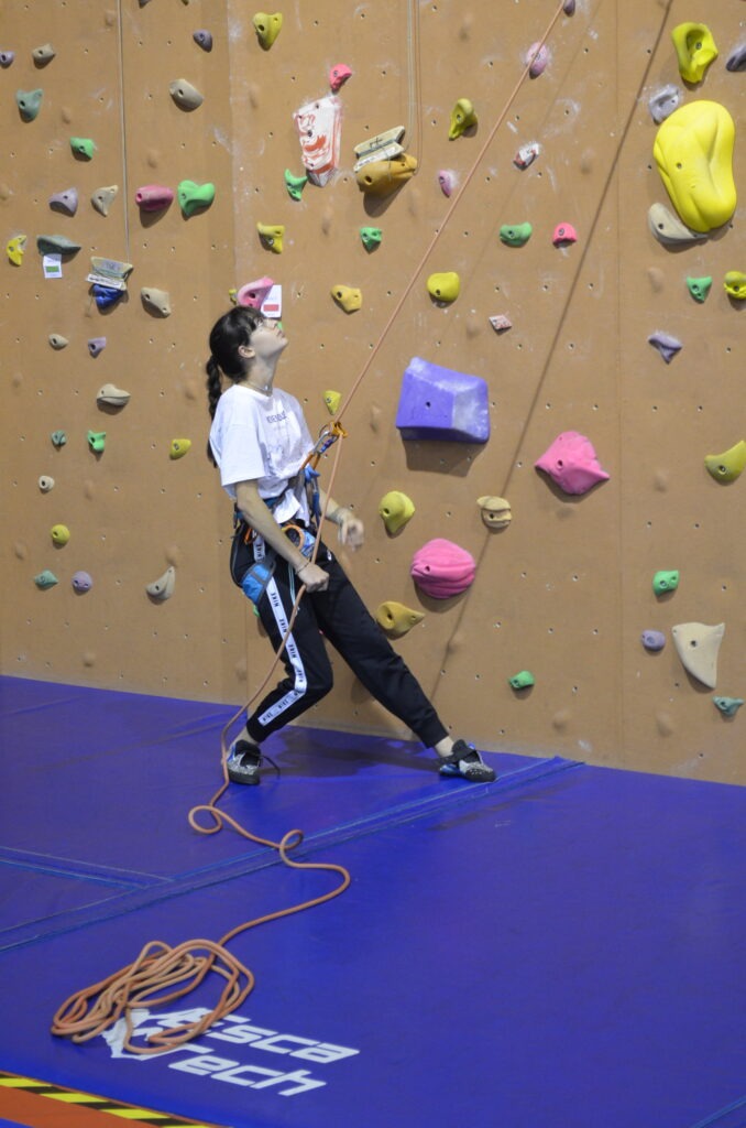 Une jeune assure un grimpeur dans un gymnase.